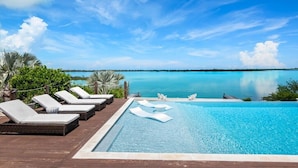 A pool with lounge chairs, a wooden deck, and a view of the ocean. - Private Beachfront Luxury Villas with Dock & Heated Pools – Perfect for 10 Guests (George Town, Exuma)