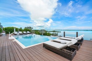 A wooden deck with a pool, lounge chairs, and a view of the sea.