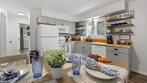 A modern kitchen with white cabinets, a wooden countertop, and a coffee bar. There is a dining table set with plates, glasses, and a centerpiece. - Family Friendly & Cheerful Blue Jay Ranch House close to KSU stadium  (Manhattan)