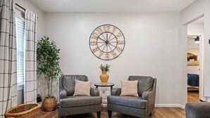A living room with two leather armchairs, a round wall clock, a small table with a vase, and a large potted plant. - Family Friendly & Cheerful Blue Jay Ranch House close to KSU stadium  (Manhattan)