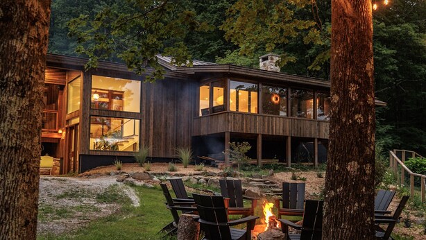 Een modern huis met grote ramen, een terras en een vuurkorf met stoelen.