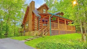 Eine Blockhütte mit Veranda, einer Treppe und Blick auf den umliegenden Wald.