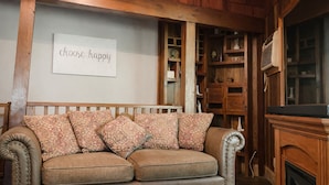 A cozy living room with a wooden ceiling, a beige sofa with patterned cushions, and a 'choose happy' sign on the wall.