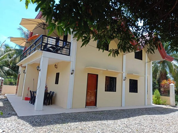 A two-story building with a balcony, a door, and a small table with chairs outside.