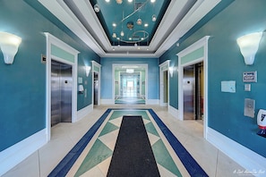 Un hall d’hôtel aux couleurs turquoise, avec un tapis noir et un sol orné de motifs géométriques.