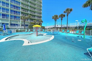 Un espace piscine d’hôtel comprenant une fontaine circulaire, des chaises longues et des palmiers.
