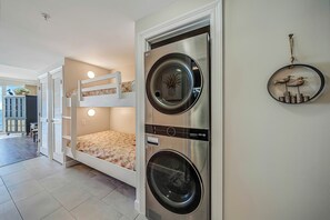 Een compacte kamer met een stapelbed, een wasmachine en een klein plankje met decoratieve spullen.