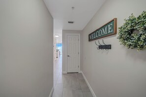 Een gang met een 'WELCOME' bord, een kapstok en een krans aan de muur.