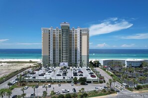 Un grand hôtel avec de nombreux étages, doté d’un parking à l’avant, offrant une vue sur une plage et l’océan.