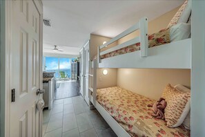 Een slaapkamer met stapelbed en uitzicht op een balkon, een deur met hendel en een plafondventilator.