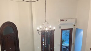 Ein geräumiger Raum mit einer Chandelüster, einer Holztür, einer weißen Wand und einem Schreibtisch mit Stuhl.