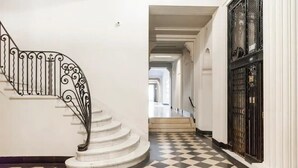 Eine Treppe mit aufwendiger Metallrelingung führt zu einem Flur mit Schachbrettfußboden und einem schwarzen Tor.
