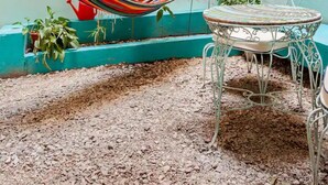 Eine Hängematte, ein Metallstuhl und ein kleiner Tisch in einem Innenhof mit grüner Wand und Pflanzen.