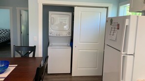 A compact kitchen with a built-in washer and dryer, a refrigerator, and a dining area with a wooden table and chairs.