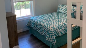 A bedroom with a bed, a ceiling fan, an air conditioning unit, a window with blinds, and a wooden floor.