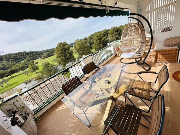 A terrace with a glass table, wicker chairs, and a view of a green landscape. - FLAT Surrounded by nature, with pool, and beach nearby (ES MERCADAL MENORCA)