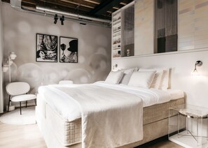 A modern bedroom with a large bed, a side table, a chair, and a wall-mounted shelf with decorative items. - Cousins Boutique Hotel (Maastricht)