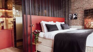 A modern bedroom with a red headboard, a large bed, a bedside table with a vase of flowers, and a brick wall.