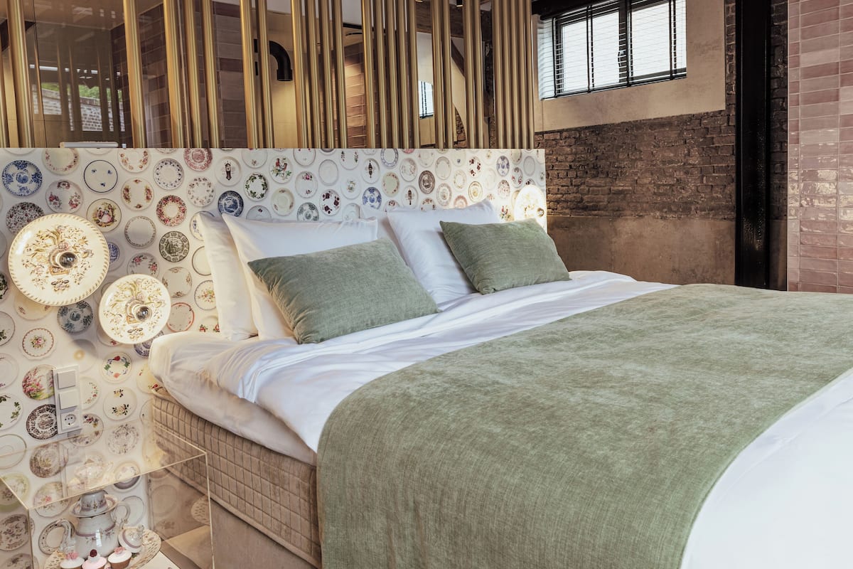 A modern bedroom with a patterned headboard, a green throw blanket, and a bedside table with decorative items.
