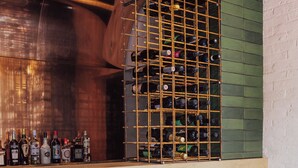 Zona de bar con botellero, dos taburetes y un revestimiento de azulejos verdes.