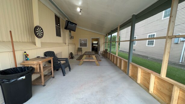 A covered outdoor area with a dartboard, a television mounted on the wall, and a table with chairs.