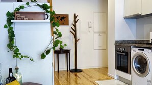 Eine moderne Küche mit Waschmaschine, Holzboden und einem grauen Sofa mit gelbem Kissen.