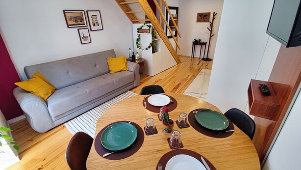 Ein modernes Wohnzimmer mit grauem Sofa, einem Holzespeisetisch für zwei Personen und einer Treppe, die zu einer oberen Ebene führt.
