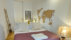 Ein ordentlich eingerichtetes Schlafzimmer mit einem Bett, einer Weltkarte an der Wand, einer Lampe und einer an der Wand stehenden Leiter.