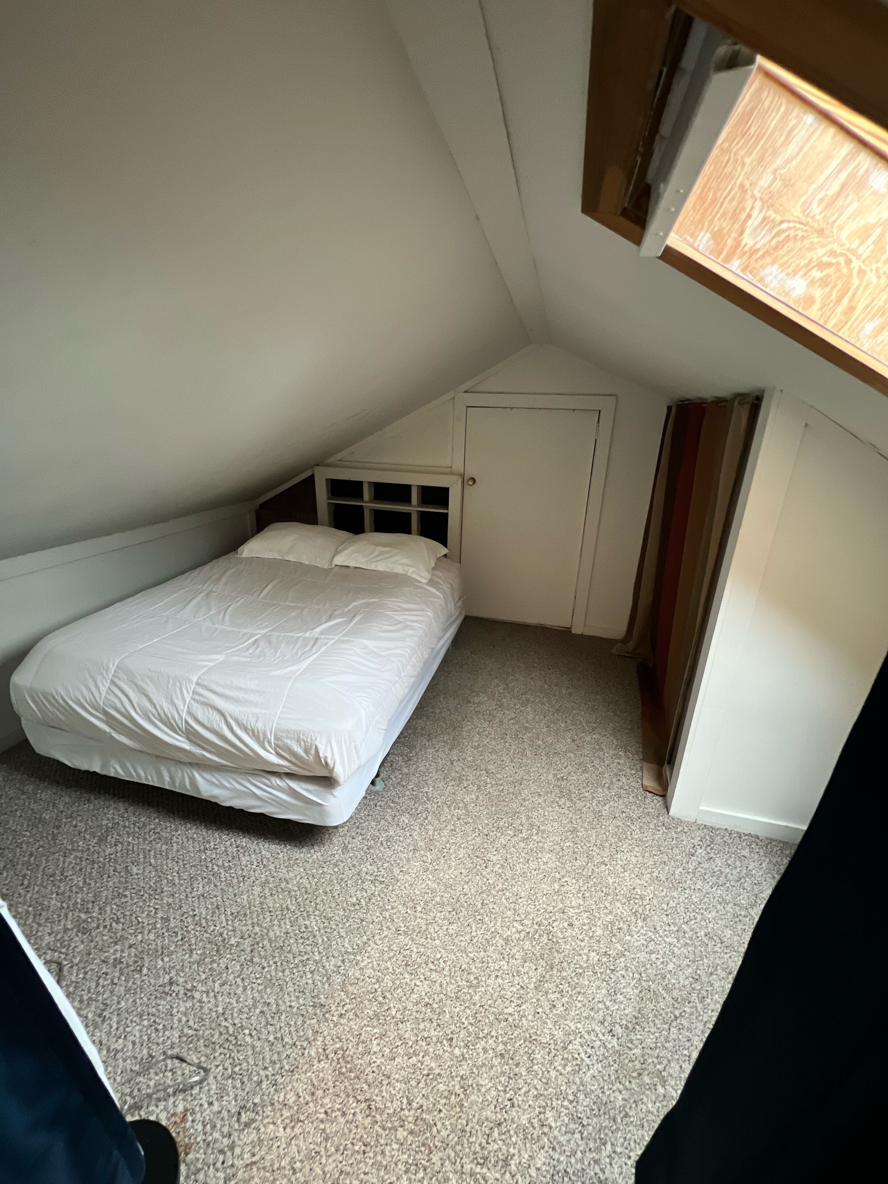 Een kleine kamer met een enkel bed, schuine wand en een raam.
