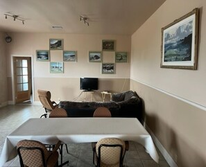 A dining area with a table and chairs, a sofa, a television, and framed pictures on the wall. - Hôtel Motel de la Minganie (Longue-Pointe-de-Mingan)