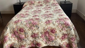 Una cama con colcha floral, dos mesitas de noche con lámparas, y suelo de madera.