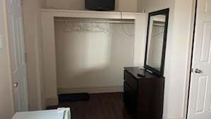 Un dormitorio con cama, tocador, espejo, televisor sobre una estantería y una puerta.