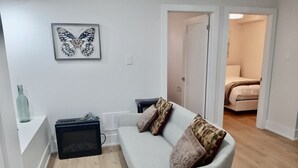A living room with a grey sofa, a framed butterfly artwork, a small table with a bottle, and a radiator. - Stylish, spacious, and bright 2-bedroom furnished basement apartment (Toronto)