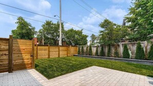 A backyard with a wooden fence, a paved patio, and a grassy area. - Stylish, spacious, and bright 2-bedroom furnished basement apartment (Toronto)