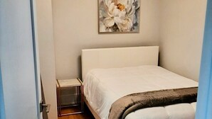 A bedroom with a bed, a bedside table, a lamp, and a painting on the wall. - Stylish, spacious, and bright 2-bedroom furnished basement apartment (Toronto)