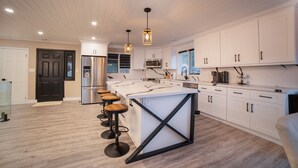 Een moderne keuken met witte kastjes, een centraal eiland met krukken, roestvrijstalen apparatuur en hanglampen.