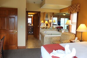 Habitació d'hotel amb un llit gran, zona de seients amb un sofà, taula petita i bany amb banyera i mirall.