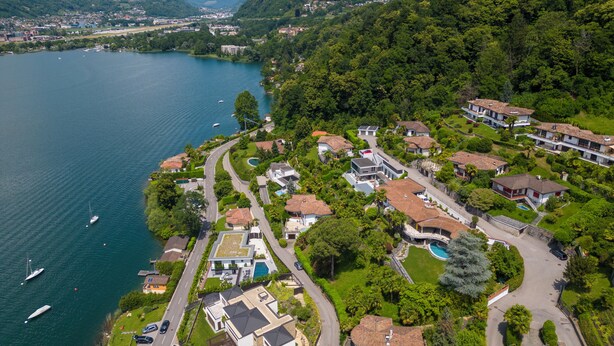An aerial view of a lakeside residential area with houses, a road, and boats on the water.