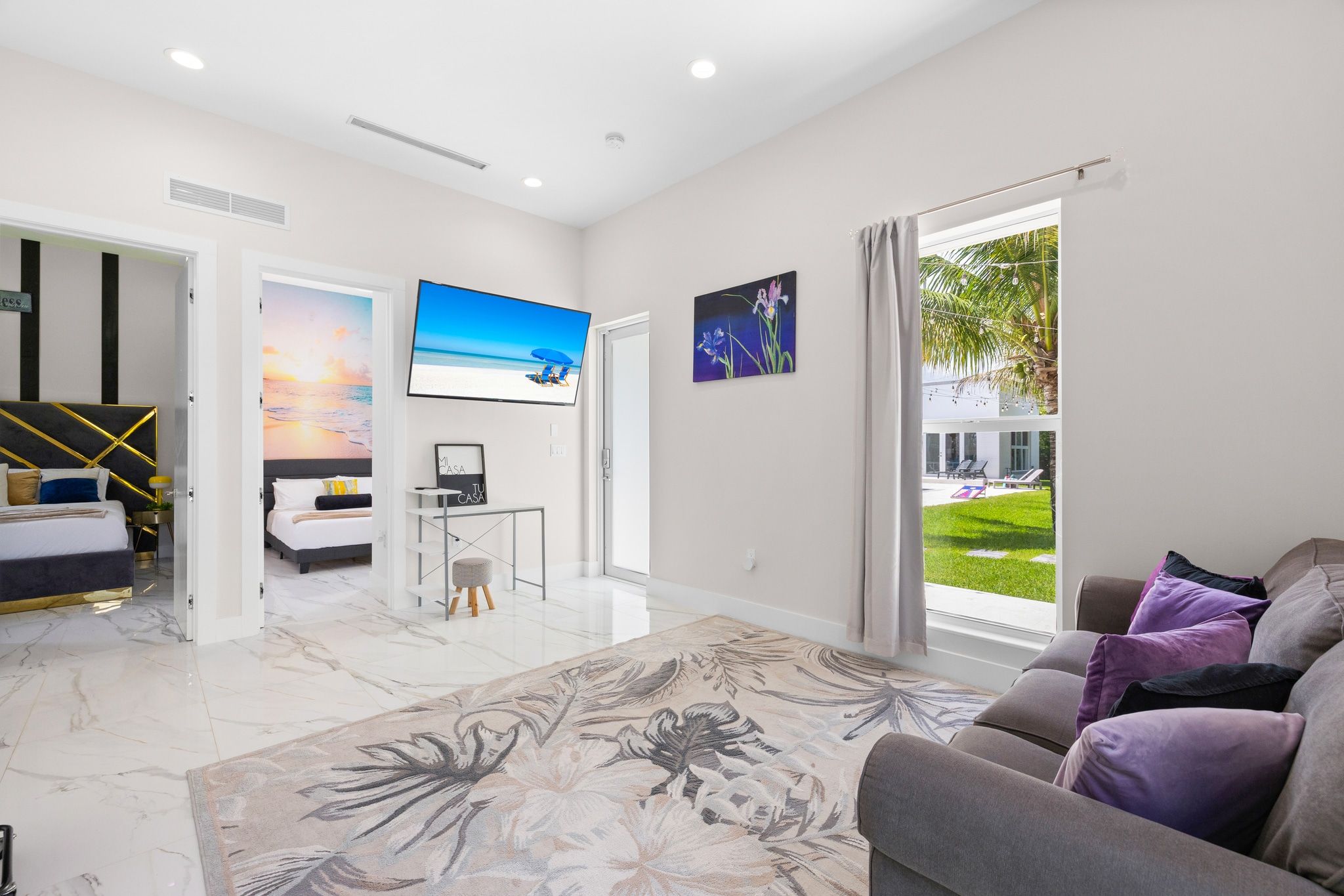 A modern living room with a large flat-screen TV, a sofa, a coffee table, and a view of a garden through a large window.