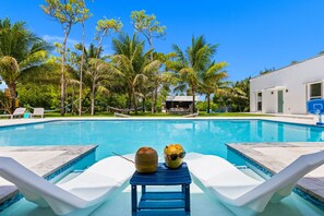 A swimming pool with lounge chairs and a small table with coconuts.