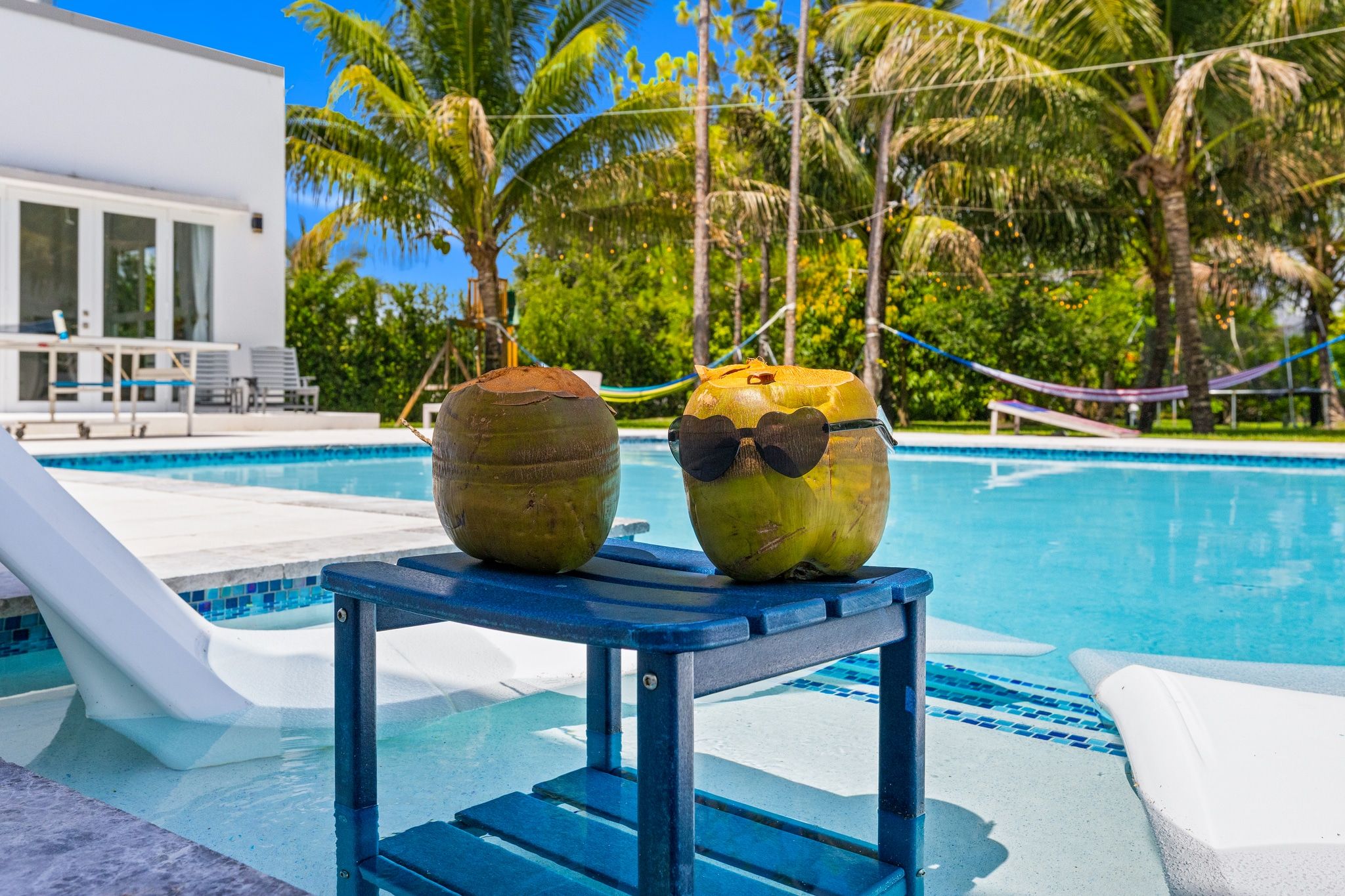 A poolside area with two coconuts on a table, a pool, and a building in the background.