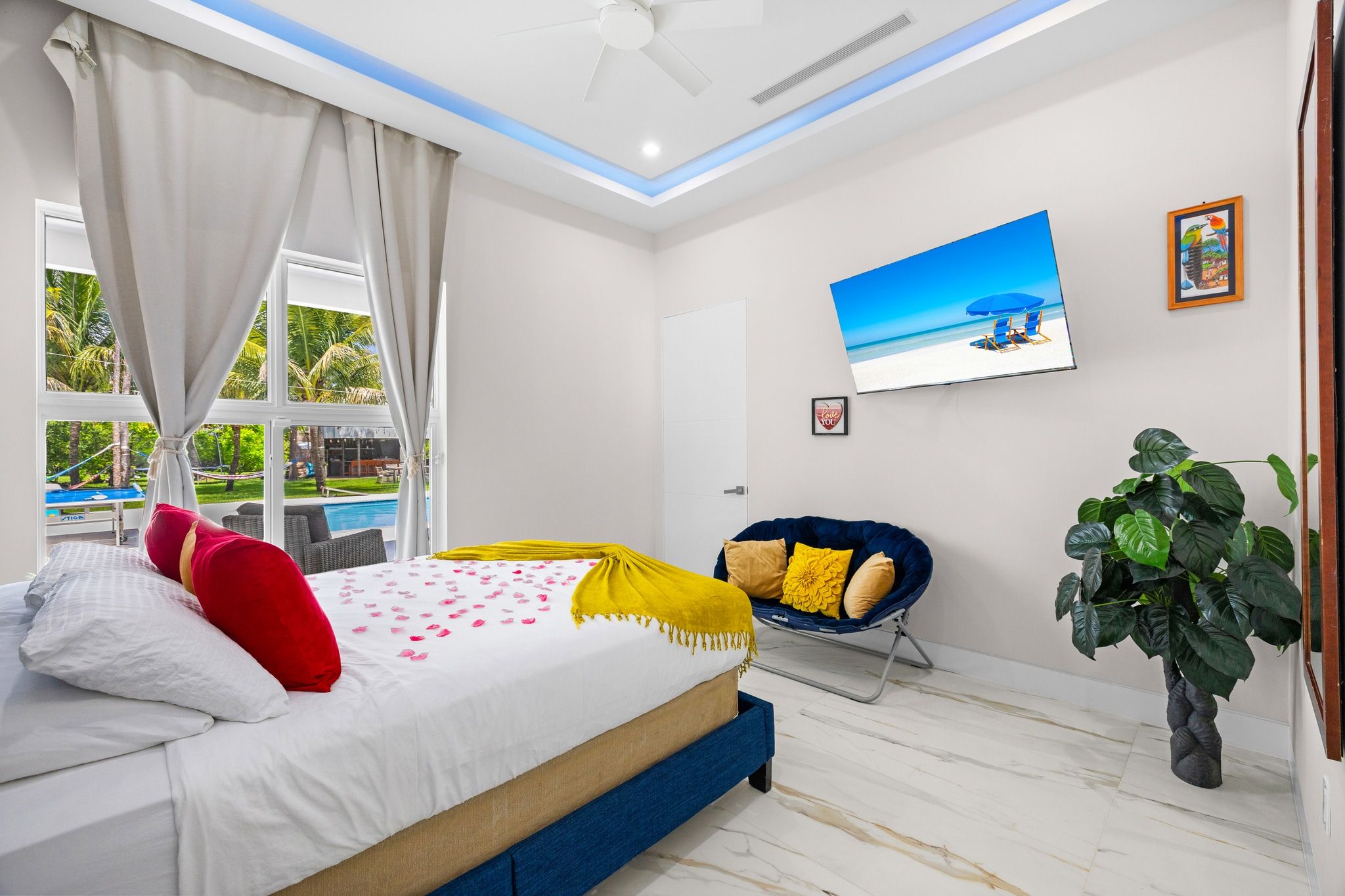 A bedroom with a bed, a chair, a potted plant, and a painting on the wall.
