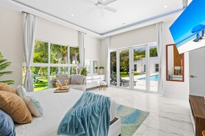A spacious bedroom with a large bed, a view of a swimming pool, and a ceiling fan.