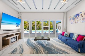 A modern living room with a television, a sofa, a coffee table, and a view of a pool and outdoor area.