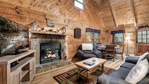A cozy log cabin interior with a stone fireplace, wooden furniture, and a dining area. - Cozy Mountain Retreat w/hot tub, 5 mins to downtown strip (Sevierville)