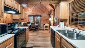 A wooden cabin interior with a kitchen featuring a stove, sink, and dining area with chairs and a table. - Cozy Mountain Retreat w/hot tub, 5 mins to downtown strip (Sevierville)