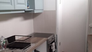 Et kompakt køkken med lyseblå skabe, en stålvask, en komfur og et flisebeklædt bagpanel.