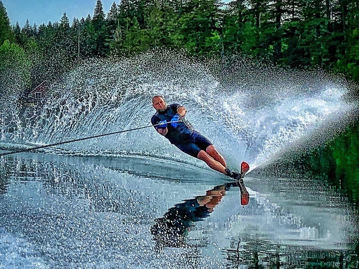 Una persona esquiando sobre el agua en un lago, con árboles al fondo.