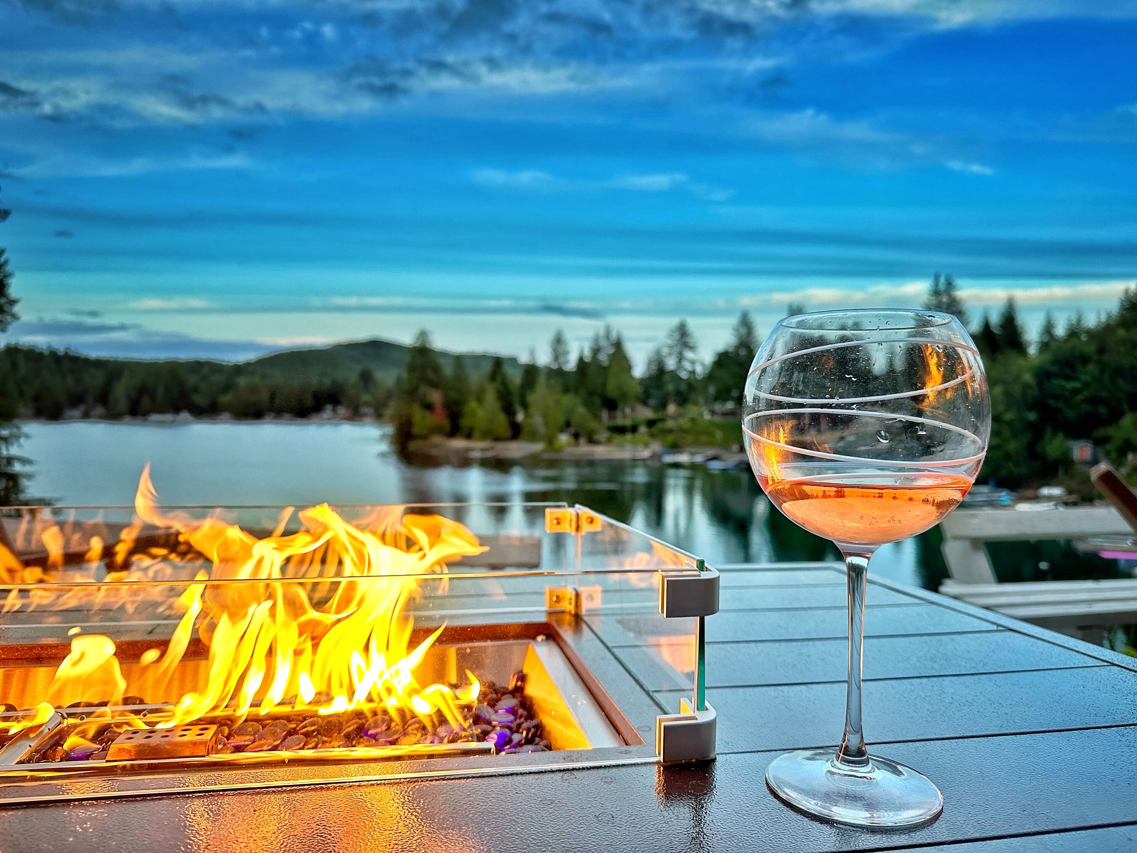 Un verre de vin sur une table, avec un foyer à proximité et une vue sur un lac et des montagnes.