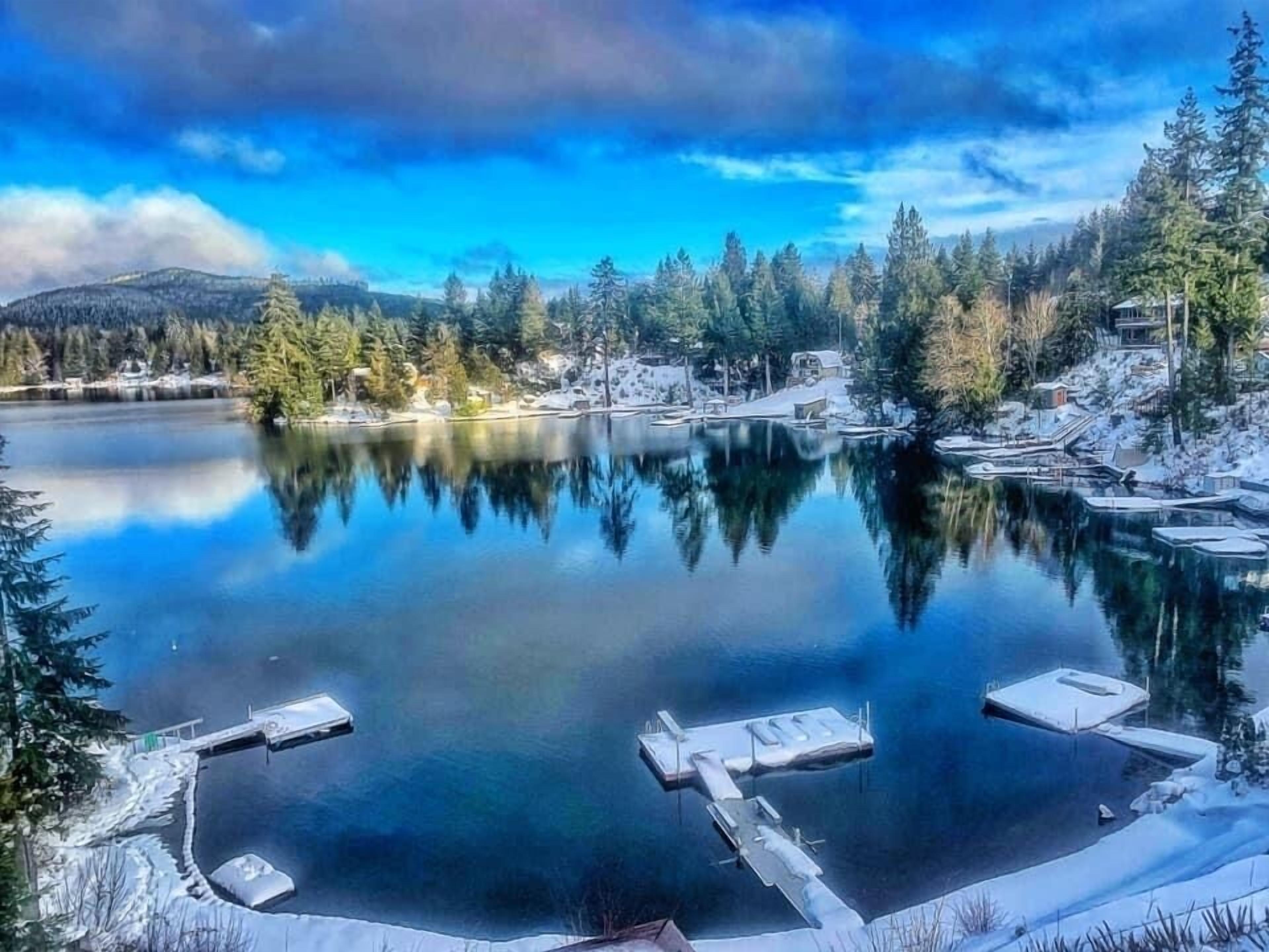A serene lake with docked boats, surrounded by snow-covered trees and a clear sky.